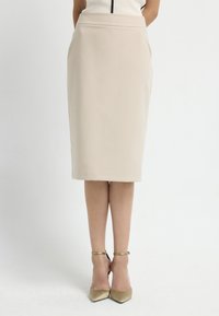 Beige Bleistiftrock mit figurbetonter Passform, knielang, glatter Textur und dezentem Glanz, kombiniert mit goldenen Riemchen-Heels.