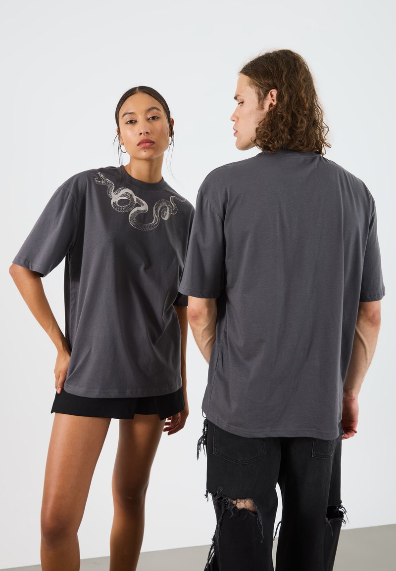 T-shirt oversize grise avec un graphique de serpent sur le devant. Manches courtes et coupe décontractée, fabriqué en coton doux.