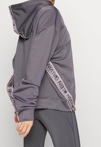 Gray athletic hoodie with a large hood. Features a side panel with a patterned trim and ribbed cuffs. Smooth texture, casual fit.