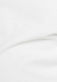 Gros plan sur un tissu blanc doux avec des plis lisses et une légère texture visible sous un éclairage doux.