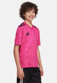 Roze synthetisch T-shirt met korte mouwen en een V-hals, voorzien van een geometrisch patroon en zwarte accenten, waaronder drie strepen op de schouders.