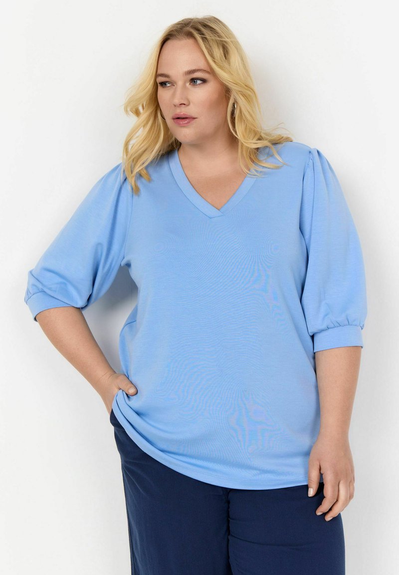 Világoskék V-nyakú blúz puffos ujjakkal, puha anyagból készült. A póló kényelmes fazonú, sima textúrával rendelkezik.