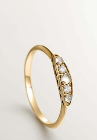 Anillo de oro con una banda lisa, que presenta tres piedras preciosas blancas y dos pequeños diamantes en un engaste pulido. Los detalles incluyen un diseño recortado.