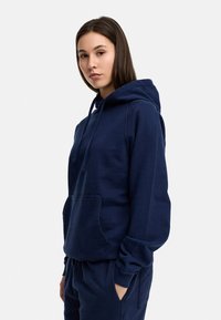 Navy blue hooded sweatshirt made of cotton blend; features a front pocket, drawstrings, and ribbed cuffs. Soft texture, casual design.