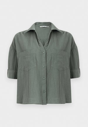 Chemise à manches courtes avec boutons sur le devant, de couleur verte atténuée, dotée de deux poches poitrine et d'un col classique, présentée sur un fond blanc.