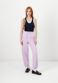 Navy tank top with white trim, paired with light purple, loose-fitting trousers and black loafers. Simple shoulder bag as an accessory.