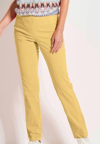 Geel broek met een rechte pasvorm, uitgerust met voorzakken en een gladde textuur, gecombineerd met een gemusterde top en witte sneakers.