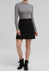 Grijze geribbelde top met lange mouwen, gecombineerd met een zwarte suedine A-lijn rok met voren knopen en zwarte veterlaarsjes tot de enkel.