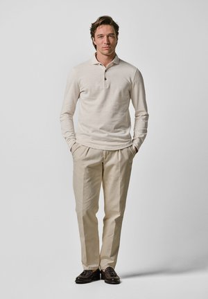 Lichtbeige polo-shirt met lange mouwen en drie knopen, gecombineerd met crèmekleurige broeken en donkerbruine instappers. Eenvoudige, op maat gemaakte pasvorm.