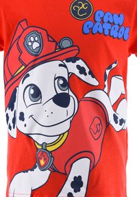 Rode katoenen t-shirt met een cartoonhond in een brandweeroutfit, met zwarte vlekken, een gele kraag en de tekst 'Paw Patrol' in het blauw.