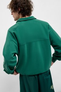 Roheline, tekstuuriga särgiga tõmbav pullover, millel on krae ja allapoole langenud õlad. Omab seam detaili seljaosas ja laia lõikega, koos sobivate pükstega.