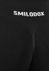 Zwarte leggings met de witte merknaam "SMILODOX" prominent weergegeven op de tailleband, met een gladde, aansluitende textuur.