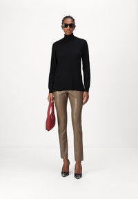 Svart turtleneck-genser, brune skinnbukser av kunstlær, svarte høye hæler, og en rød håndveske. Modellen har på seg svarte solbriller.
