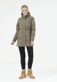 Olivgrön, huva parka med midjesnörning, två zipprade bröstfickor och elastiska ärmar, parat med svarta byxor och bruna stövlar.