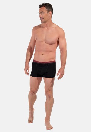 Zwarte boxershorts met een bordeauxrode elastische tailleband met logodetail. De pasvorm is aansluitend met een zachte stoftextuur. Model staat met blote voeten.