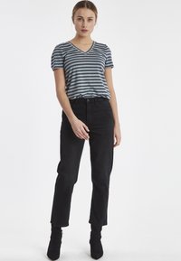 Gestreepte V-hals t-shirt in grijs en blauw, gecombineerd met hoge zwarte jeans. Outfit compleet met zwarte enkellaarsjes. Model poseert rechtop.