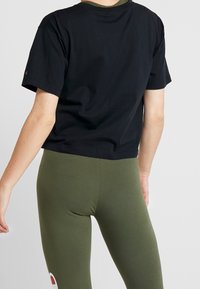 Černé bavlněné tričko s krátkým rukávem a kulatým výstřihem, minimalistického designu, v kombinaci se zelenými legínami s akcentním detailem.