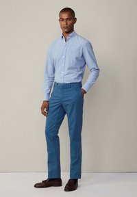 Jasnoniebieska koszula z kołnierzykiem, w połączeniu z turkusowymi spodniami. Brązowe mokasyny dopełniają stylizację, podkreślając smart-casualowy wygląd.