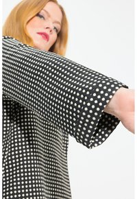 Tissu noir avec des pois blancs, comportant un large poignet et un design texturé. La manche s'avance, mettant en valeur le motif.