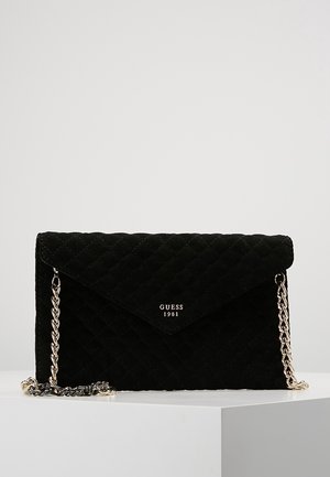Czarna pikowana torba na ramię z złotym łańcuszkiem i logo „GUESS 1981” na przedniej klapce, wyświetlona na białej powierzchni.