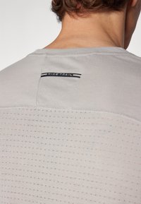 Light grey Nike Trail t-shirt with a breathable, textured back and stitched detailing. Features a small label at the upper back.