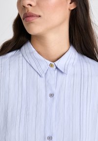 Lichtblauw shirt met dunne verticale strepen, een klassieke kraag en een knoopsluiting met een goudkleurige accent. Gestructureerde stof.