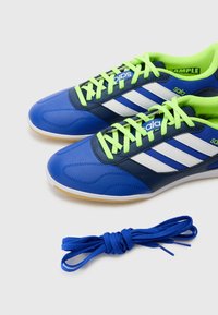 Blauwe en marineblauwe sportschoenen met witte strepen en felgroene veters. Inclusief een geknoopte blauwe veter die naast de schoenen ligt.