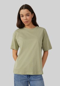 T-shirt en coton vert clair avec une coupe décontract�ée, des manches courtes et un col rond, associé à un jean en denim bleu.