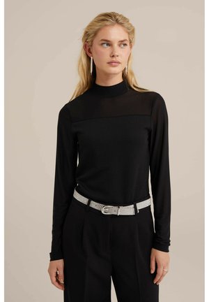 Zwarte langemouwen top met een doorschijnend bovenpaneel, ribbeltextuur, hoge halslijn, gecombineerd met hoge zwarte broeken en een riem met een zilveren gesp.