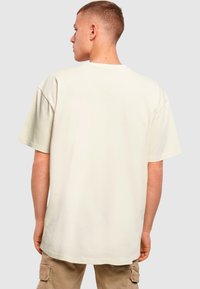 Cremefarvet oversized t-shirt med korte ærmer, rund hals og glat tekstur, vist fra bagsiden med et enkelt design.