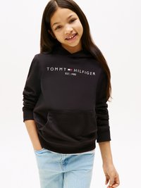 Melnā kapuce ar priekšējo kabatu un ribotām piedurknēm, ar baltu "TOMMY HILFIGER" logo un "EST. 1985.". Kombinēta ar gaiši ziliem džinsiem.