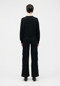 Svart strikkegenser med teksturert rygg, kombinert med svarte vide cargobukser med sidelommer. Boots med flat såle fullfører antrekket.