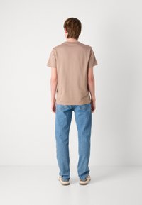 T-shirt en coton beige clair avec des manches courtes, un col rond et une coupe décontractée. Porté avec un jean en denim bleu clair et des chaussures décontractées.