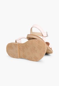 Roze sandalen met verstelbare banden, een platte zool en een reliëfvlinderpatroon op de buitenzool, met een zachte textuur.