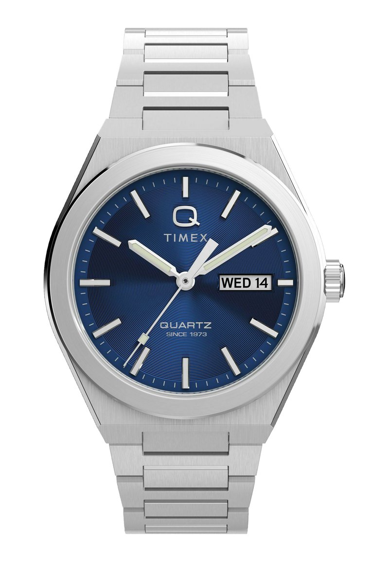 Sudraba Timex rokas pulkstenis ar zilu ciparnīcu, sudraba stundu marķieriem, luminosām rokām, sekundes rādītāju un dienas-datuma displeju, kurā ir uzraksts "CET 14".