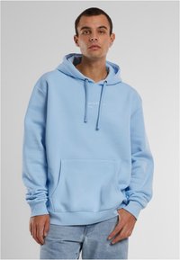 Svijetloplava dukserica s vezicama, prednjim džepom i rebrastim rukavima. Ima suptilan bijeli logo na prsima. Mekana tekstura tkanine.