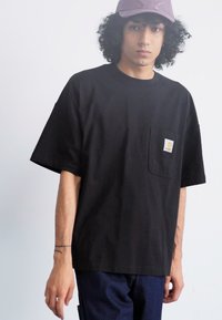 Black short-sleeve t-shirt made of cotton with a chest pocket featuring a square logo. Simple design and loose fit with a crew neckline.