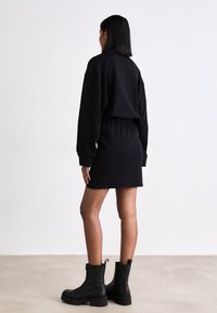 Čierne šaty so sweatshirtovým strihom, elastickým pásom, dlhými rukávmi a voľným strihom. Skombinované s robustnými čiernymi členkovými botami.