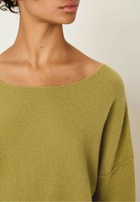 Pull en maille douce, vert olive, avec un large col bateau et des épaules tombantes. Présente une finition texturée et une coupe décontractée.