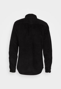 Musta vedyttävä samettipaita, jossa on kaulus, pitkät hihat ja selässä teksturoitu ribbineulos sekä pyöristetty helma.