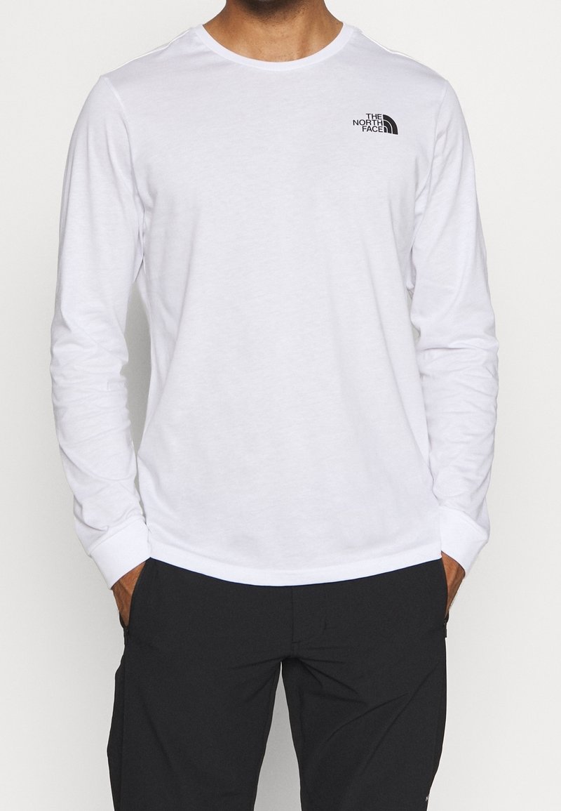 Vit långärmad skjorta i mjukt tyg, med rund halsringning och en liten svart logotyp på vänster bröst. Platta sömmar, klassisk passform.