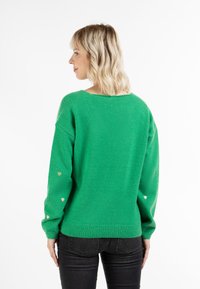 Maglione verde con vestibilità rilassata e ampio scollo. Presenta tessuto testurizzato e piccoli accenti a forma di cuore dorato sulle maniche.