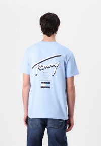 T-shirt en coton bleu clair avec un grand logo "Tommy" blanc et noir et des noms de villes en lettres gras au dos. Manches courtes, coupe décontractée.