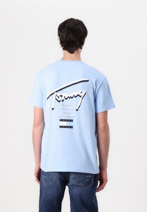 Gaiši zilas kokvilnas t-krekls ar lielu baltu un melnu "Tommy" logo un pilsētu nosaukumiem treknrakstā aizmugurē. Īsas piedurknes, brīvs piegriezums.