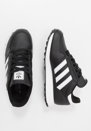 Baskets Adidas noires et blanches avec trois bandes blanches, lacets noirs et semelle blanche texturée, vues de dessus et de côté.
