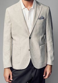 Lys beige linned blazer med en enkelt knaplukning, notchede klapkraver og to forlommer. Inkluderer et mønstret lommetørklæde.