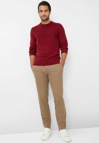 Maglione rosso a maglia con texture a coste, abbinato a pantaloni chinos beige chiaro e sneakers bianche, che mostrano una vestibilità rilassata e un design classico.