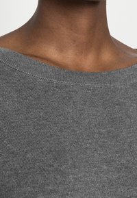 Pull en tricot gris avec un large col bardot, présentant une texture lisse et des coutures visibles le long de l'encolure.