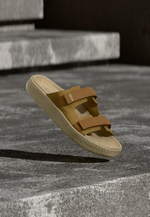 Sandali marroni con due cinturini regolabili e suola texturizzata. Realizzati in materiale morbido, presentano ritagli e un design minimalista.