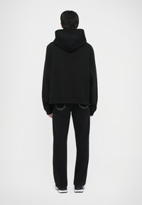 Melnā oversize kapuca, saskaņota ar melnām taisnām biksēm. Gluda tekstūra, minimāls dizains un nav redzami logotipi vai raksti.